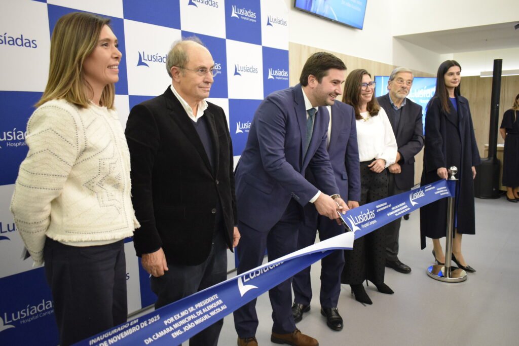 Presidente da Câmara de Alenquer corta a fita na inauguração de um novo espaço de saúde Lusíadas, acompanhado por membros da administração e representantes do Grupo Névoa, em frente ao painel institucional da marca.