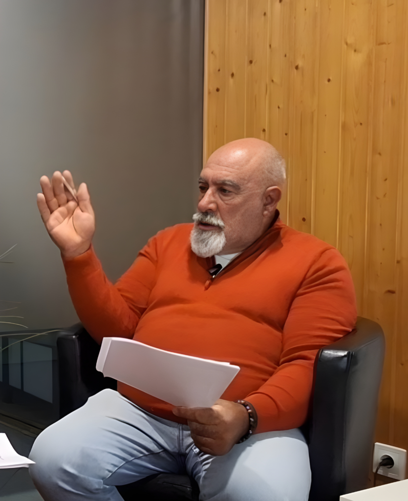 Carlos Fonte sentado durante uma entrevista, a falar e a gesticular com documentos na mão
