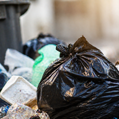 Sacos de lixo e resíduos acumulados junto a um contentor, ilustrando problemas de deposição e limpeza urbana