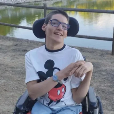 Jovem de 19 anos em cadeira de rodas, sorridente, ao ar livre junto a um lago