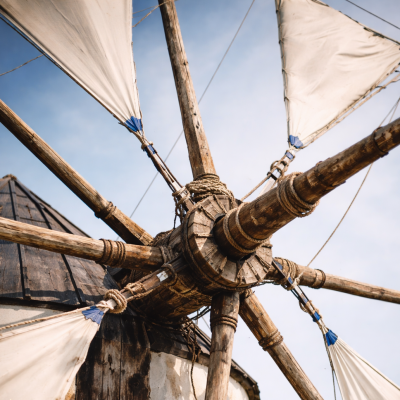 Close-up da roda e velas de um moinho tradicional, com destaque para a estrutura em madeira e os detalhes técnicos.